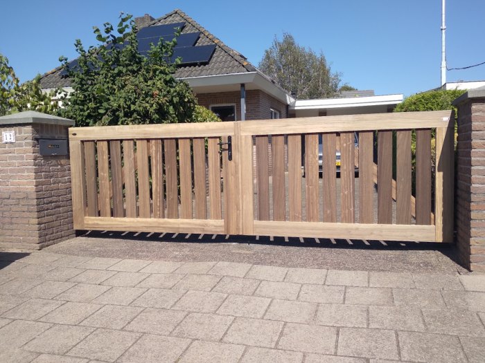 Houten tuinpoort op maat met dubbele draaideuren tussen gemetselde poeren bij vrijstaande woning